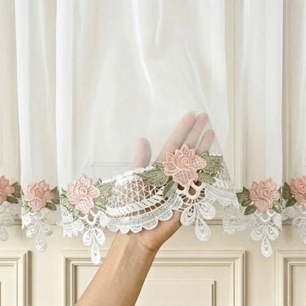 Zbliżenie na dłoń trzymającą białą satynową kokardę oraz koronkowy detal gipiury z motywem róż.