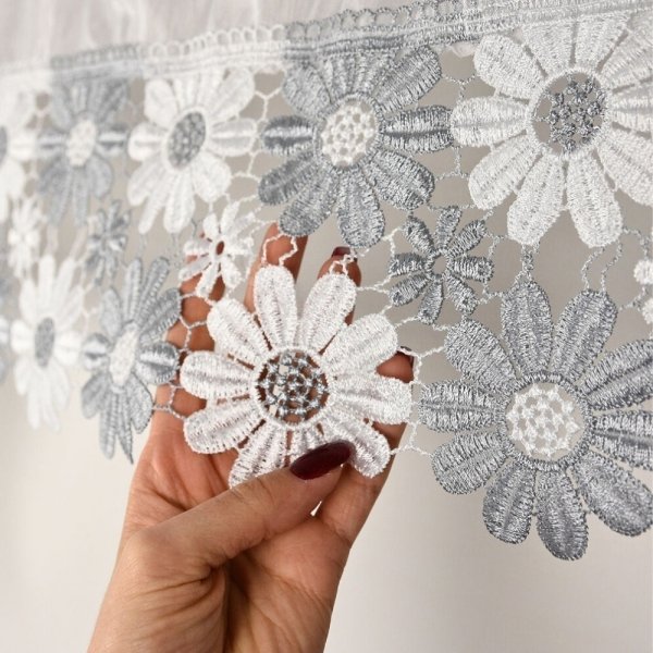 Zbliżenie na dłoń prezentującą biało-szary haft kwiatowy na tkaninie haftowanej modelu Megan.